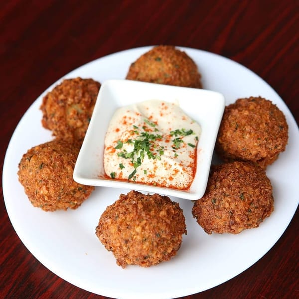 Crispy falafel balls arranged around a white dish of creamy hummus, garnished with paprika and parsley.