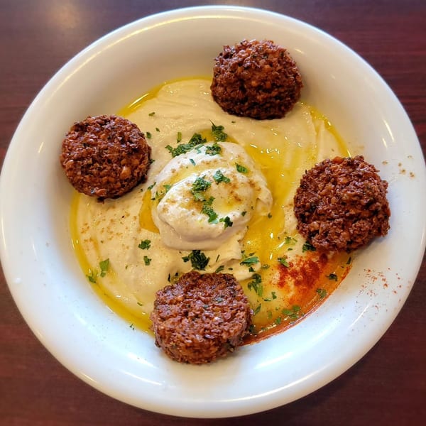 A white bowl of hummus topped with olive oil, parsley, paprika, and four falafel balls.